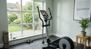 A compact Kettler cross trainer with a heart rate monitor setup in a modern British spare room featuring natural daylight and garden views.